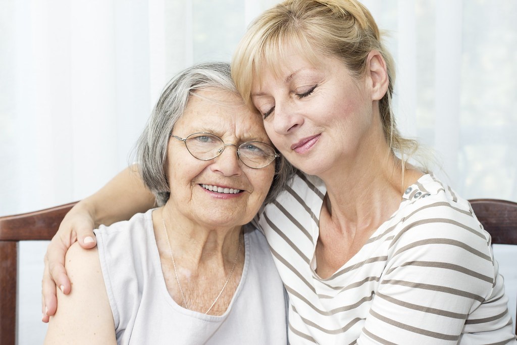 Home health aide sitting close to a smiling older woman at home, offering companionship and daily support