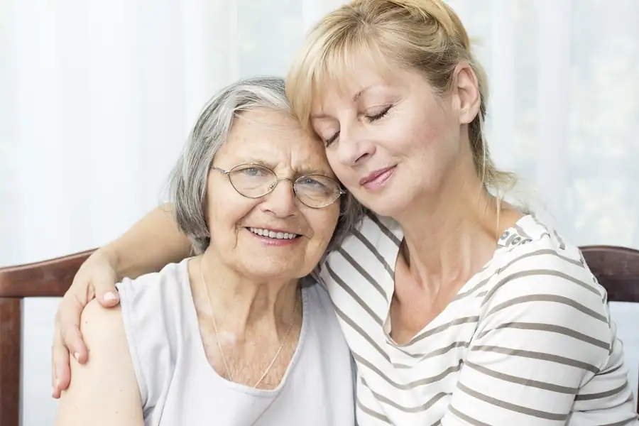 Home health aide sitting close to a smiling older woman at home, offering companionship and daily support