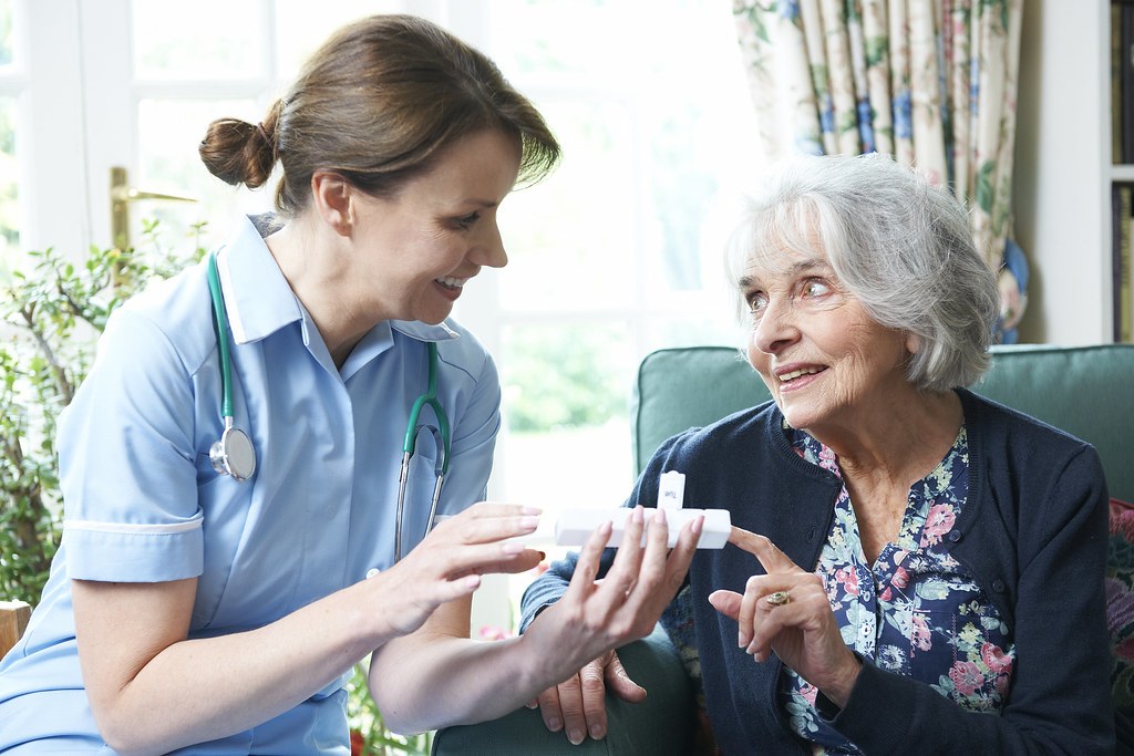 Home health nurse reviewing medications with an older woman in her living room during a home visit